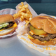 Two cheeseburgers and fries sitting in their wrapper on the hood of a car